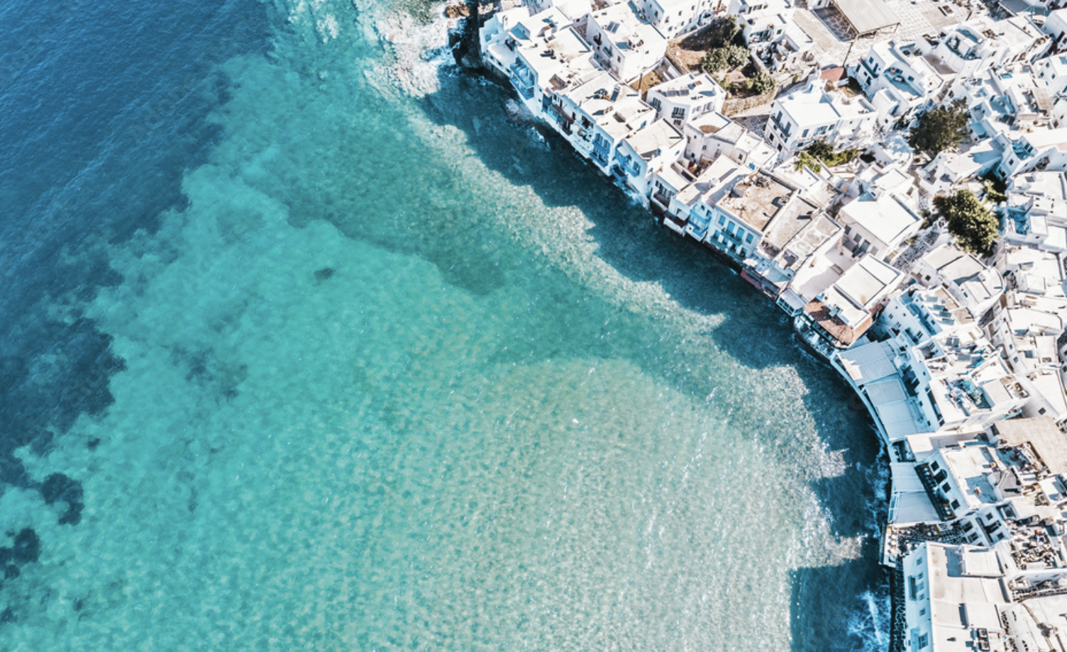 Aerial view of Mykonos coastline with luxury villas, yachts, and beach clubs during summer